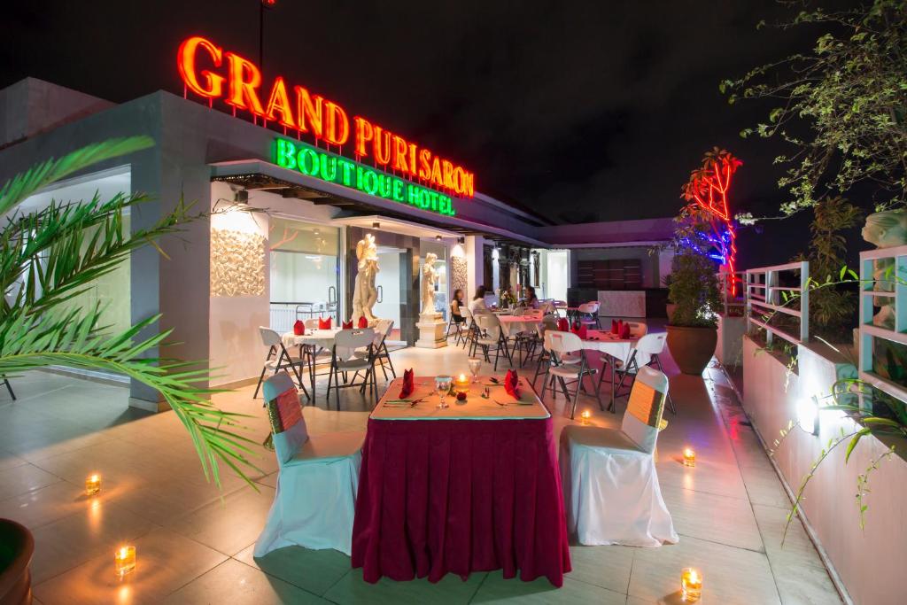 een restaurant met tafels en stoelen en een neonbord bij Grand Puri Saron Yogyakarta in Yogyakarta