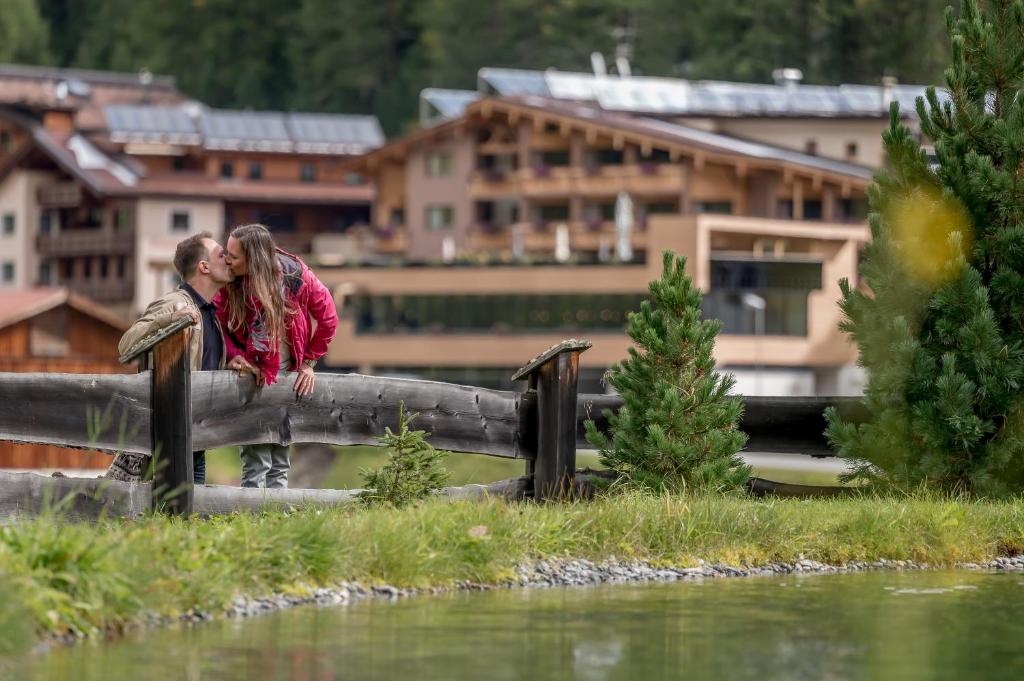 um casal a beijar-se numa ponte ao lado de um rio em 4 Sterne Superior Mühle Resort 1900 - Adults only em Obergurgl