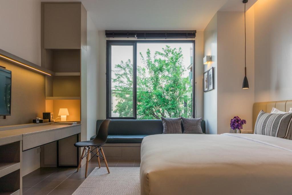 A contemporary bedroom combines a large bed, window sofa and compact desk beneath a leafy view.