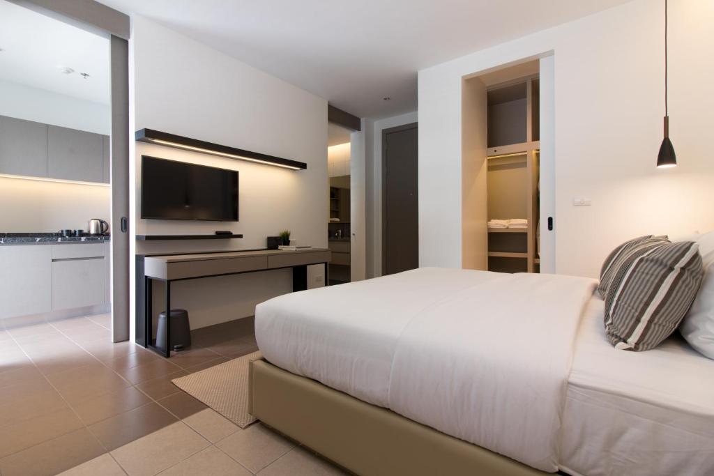 A bedroom with a large bed, TV console, kitchenette and open wardrobe.