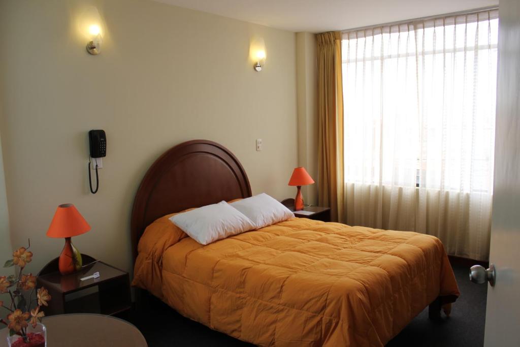 a bedroom with a bed with an orange blanket and a window at La Almohada del Rey in Arequipa