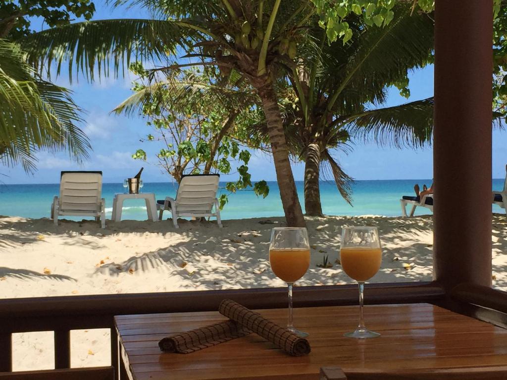 zwei Gläser Orangensaft auf einem Tisch vor dem Strand in der Unterkunft Villa Belle Plage in Anse Kerlan