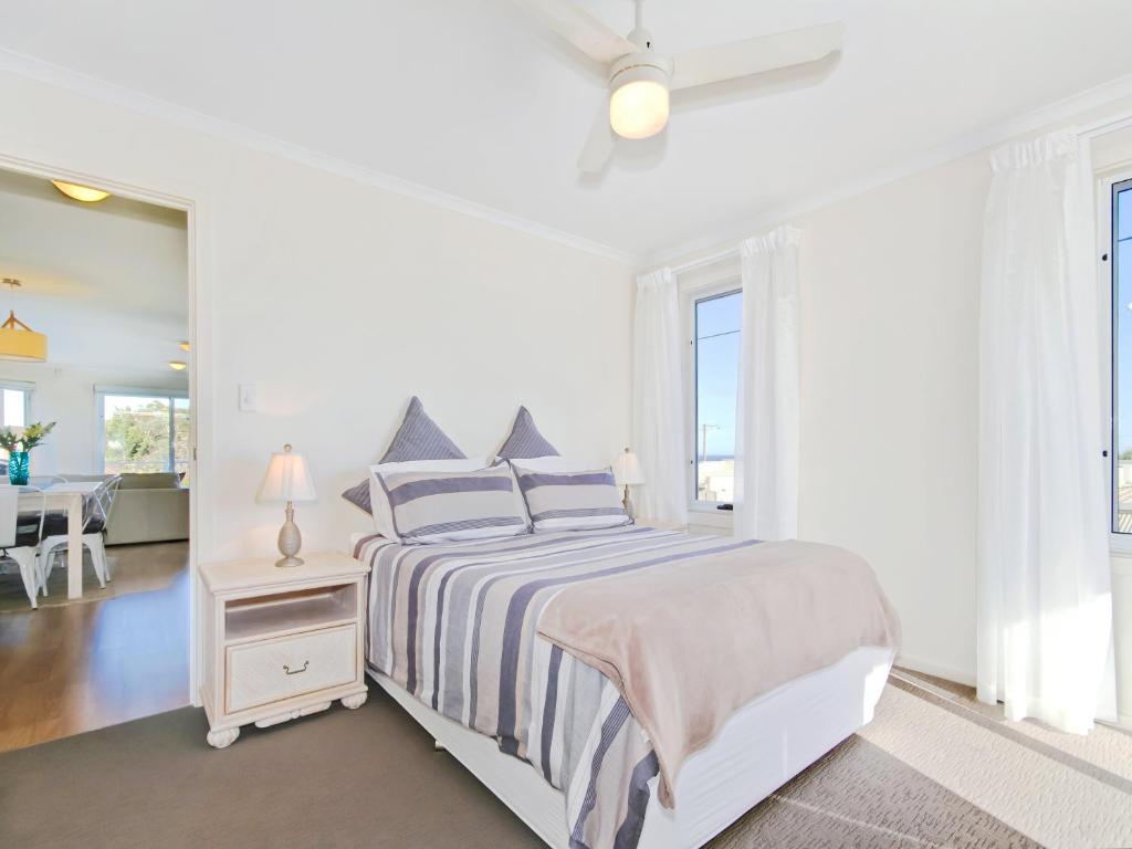 a white bedroom with a bed and a mirror at Sunset at Snapper Point - Aldinga Beach - C21 SouthCoast Holidays in Aldinga Beach