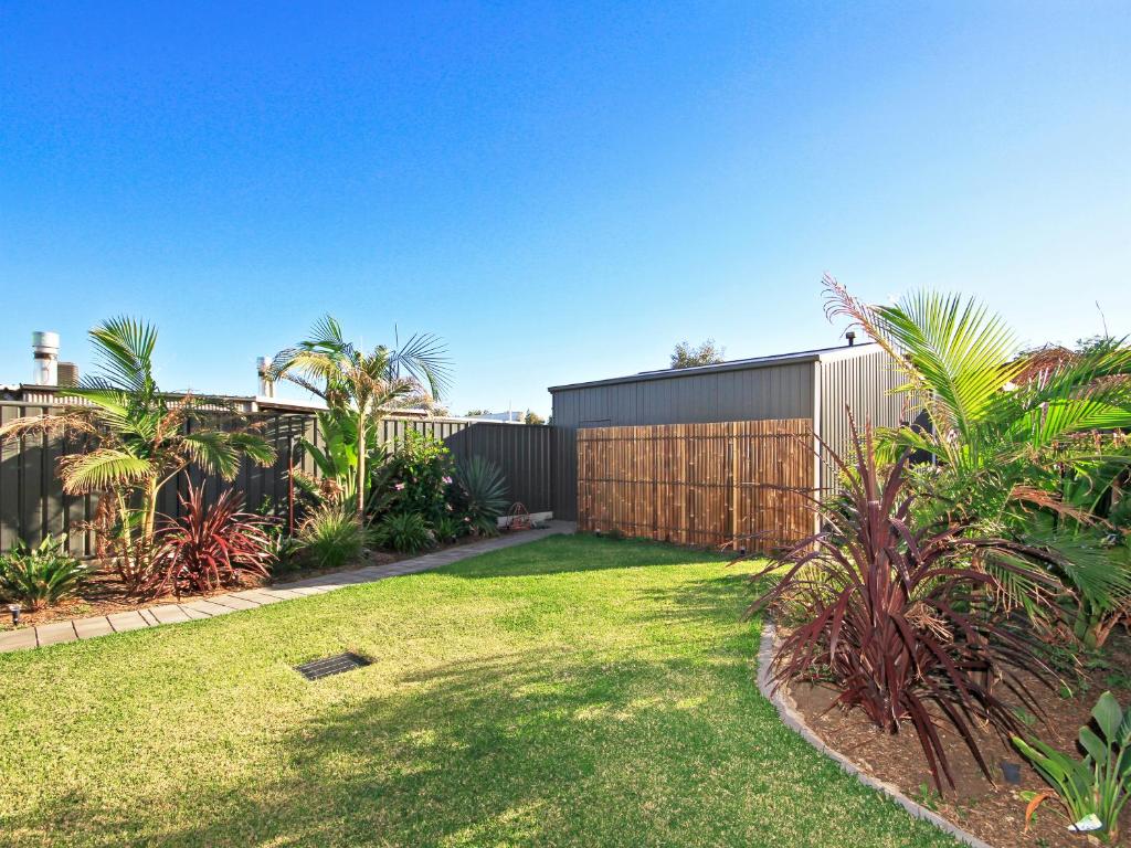 a backyard with a fence and a yard with palm trees at Sunset at Snapper Point - Aldinga Beach - C21 SouthCoast Holidays in Aldinga Beach