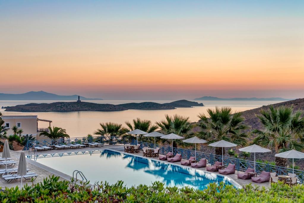 a hotel pool with chairs and umbrellas at sunset at Sunrise Beach Suites in Azolimnos Syros