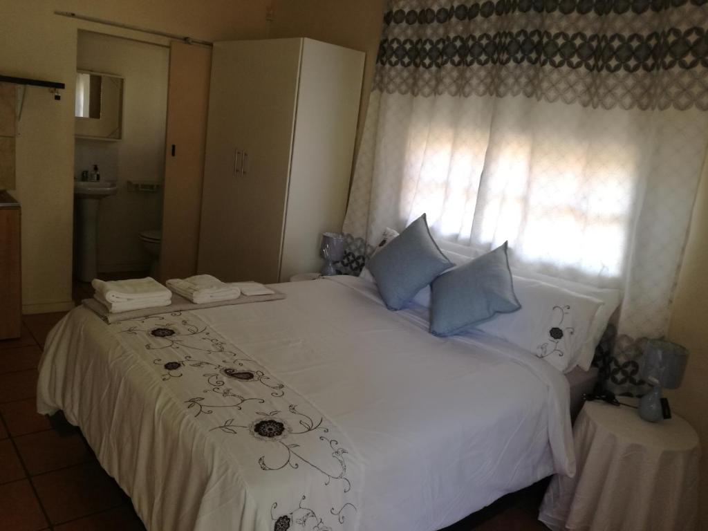 Un dormitorio con una cama blanca con almohadas azules y una ventana en MulMas Guest House, en Pretoria