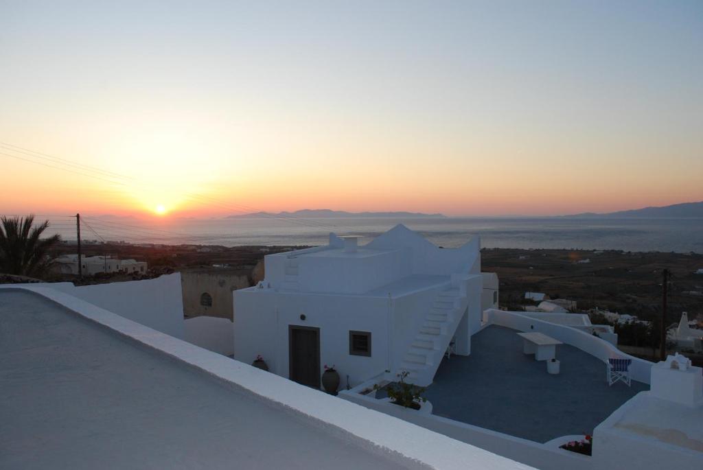 um pôr-do-sol sobre os telhados de um edifício branco em Palm Tree Hill em Oia