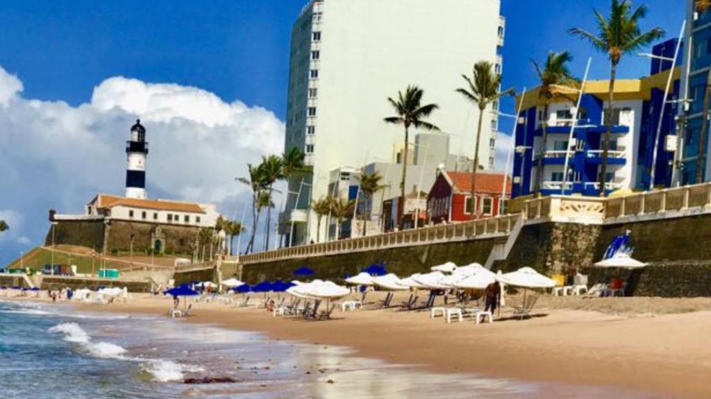a beach with chairs and umbrellas and a lighthouse at Apart Flat Farol da Barra in Salvador