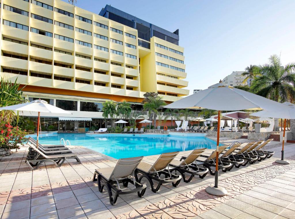 a pool with chairs and umbrellas in front of a hotel at Dominican Fiesta Hotel in Santo Domingo