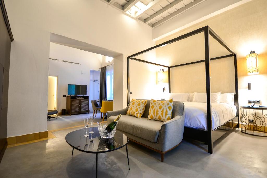 a bedroom with a bed and a couch and a table at Hotel Legado Alcazar in Seville