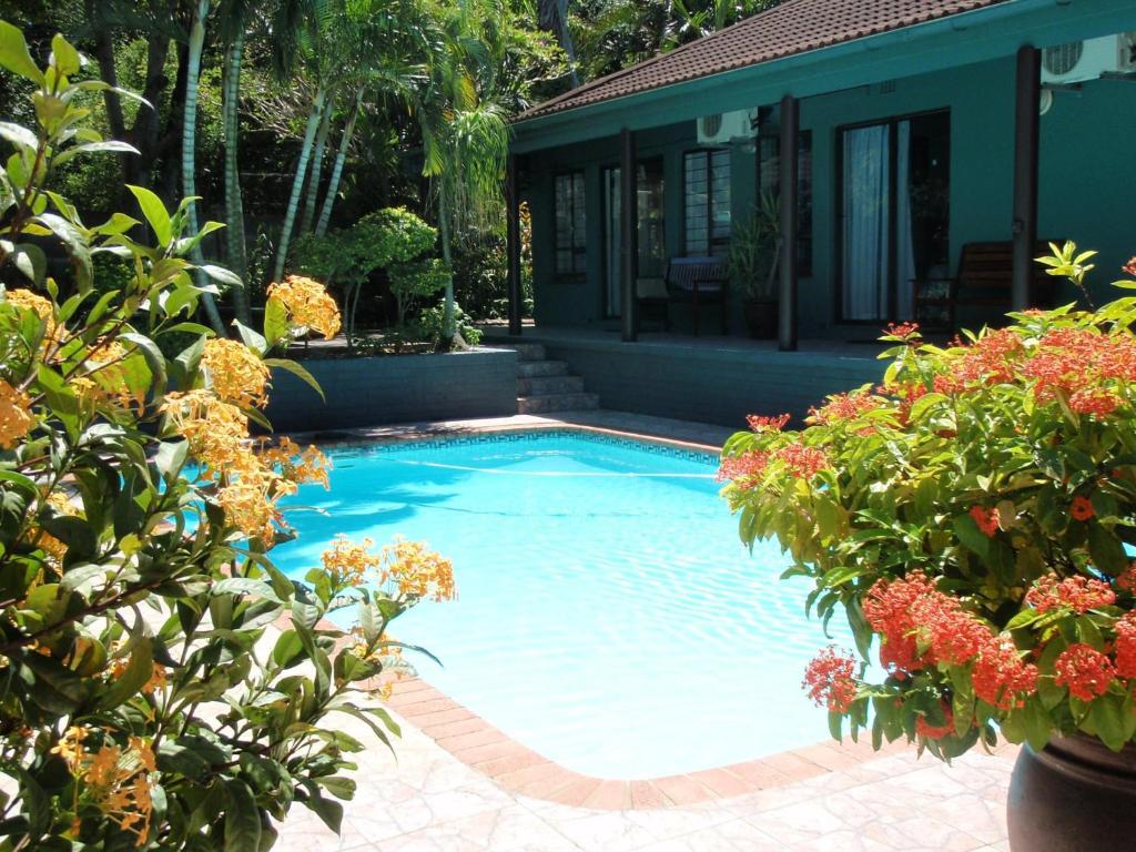 a large blue swimming pool in a yard with flowers at La Rochelle Inn in Richards Bay