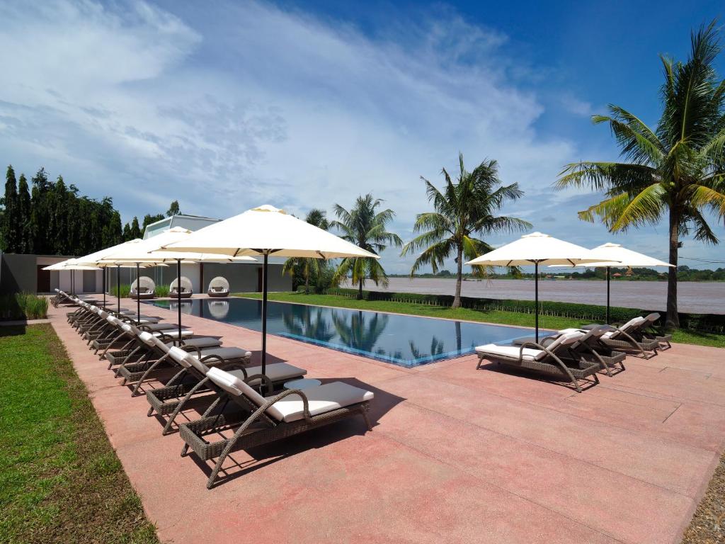 a group of lounge chairs and umbrellas next to a pool at The Bale Phnom Penh by LifestyleRetreats in Phnom Penh