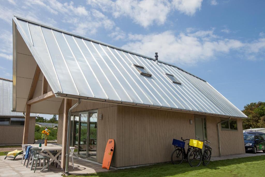 a house with a metal roof with a table and bikes at Aan Noordzee Villa Veranda in Sint Maartensvlotbrug