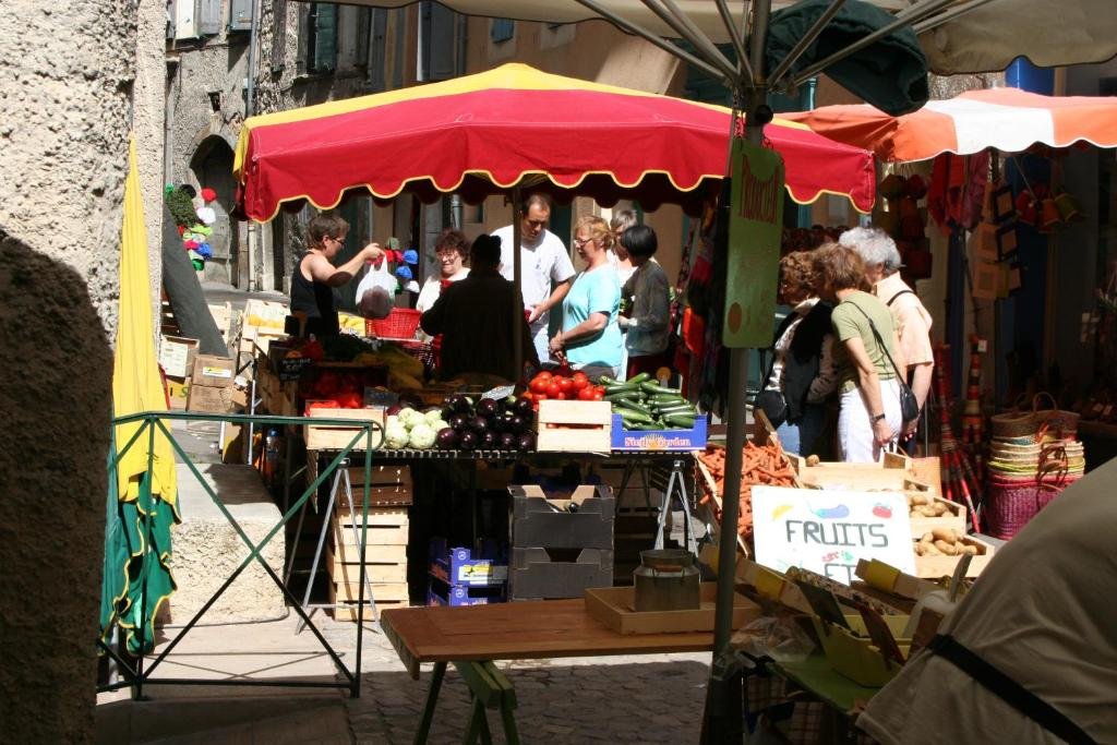 Un groupe de personnes autour d'un marché avec un parapluie rouge dans l'établissement La Maison derrière la Fontaine, à Buis-les-Baronnies