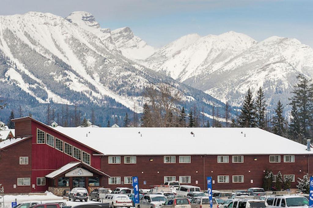 ein großes rotes Gebäude mit schneebedeckten Bergen im Hintergrund in der Unterkunft Fernie Slopeside Lodge in Fernie