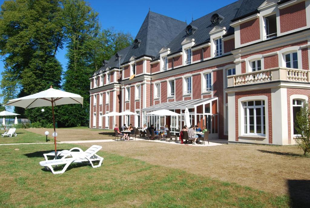 - un grand bâtiment avec des chaises et un parasol devant dans l'établissement Résidence Goélia Les Portes d'Étretat, à Maniquerville