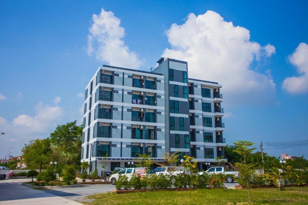 a tall white building with cars parked in a parking lot at Promsook Apartment in Bangsaen