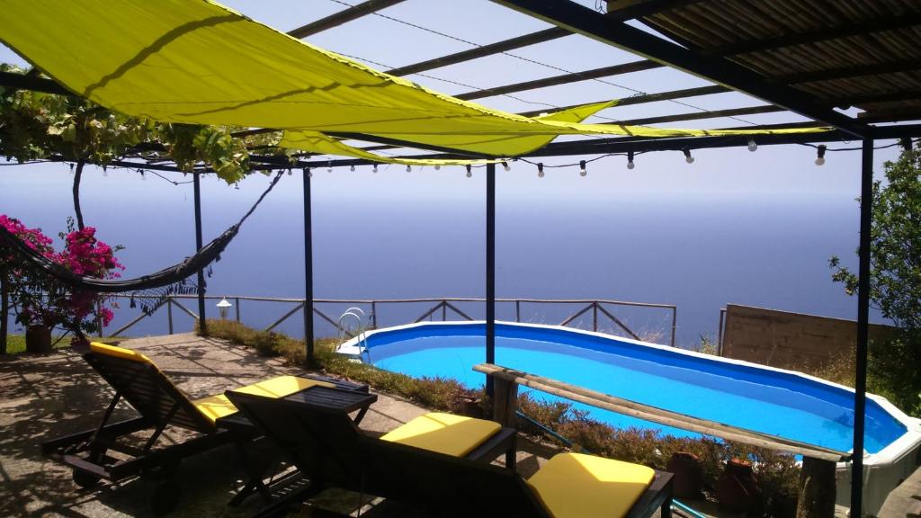 a swimming pool with chairs and an umbrella at Ocean View Cottage in Arco da Calheta