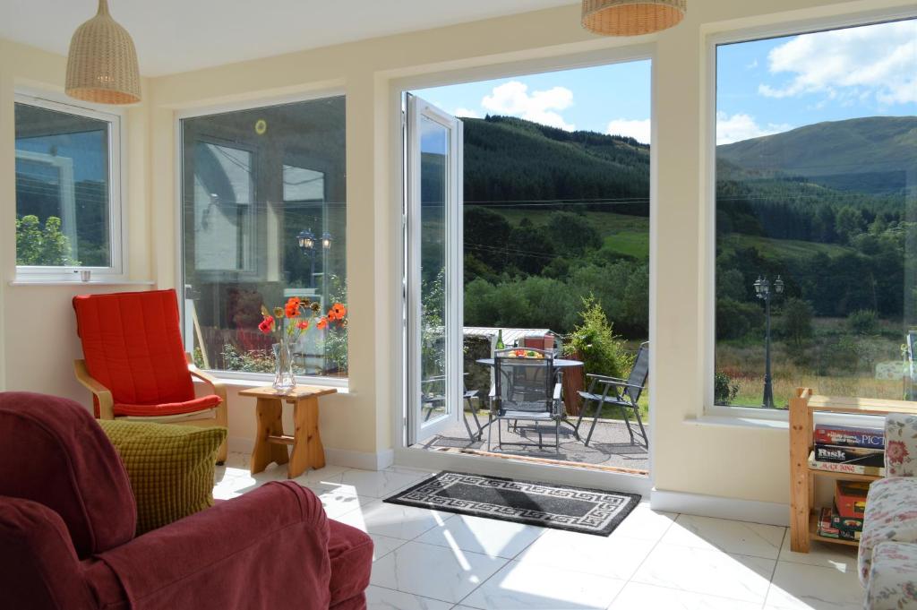 a living room with large windows and a view of the mountains at Gorsnavoon Cottage in Clachaig