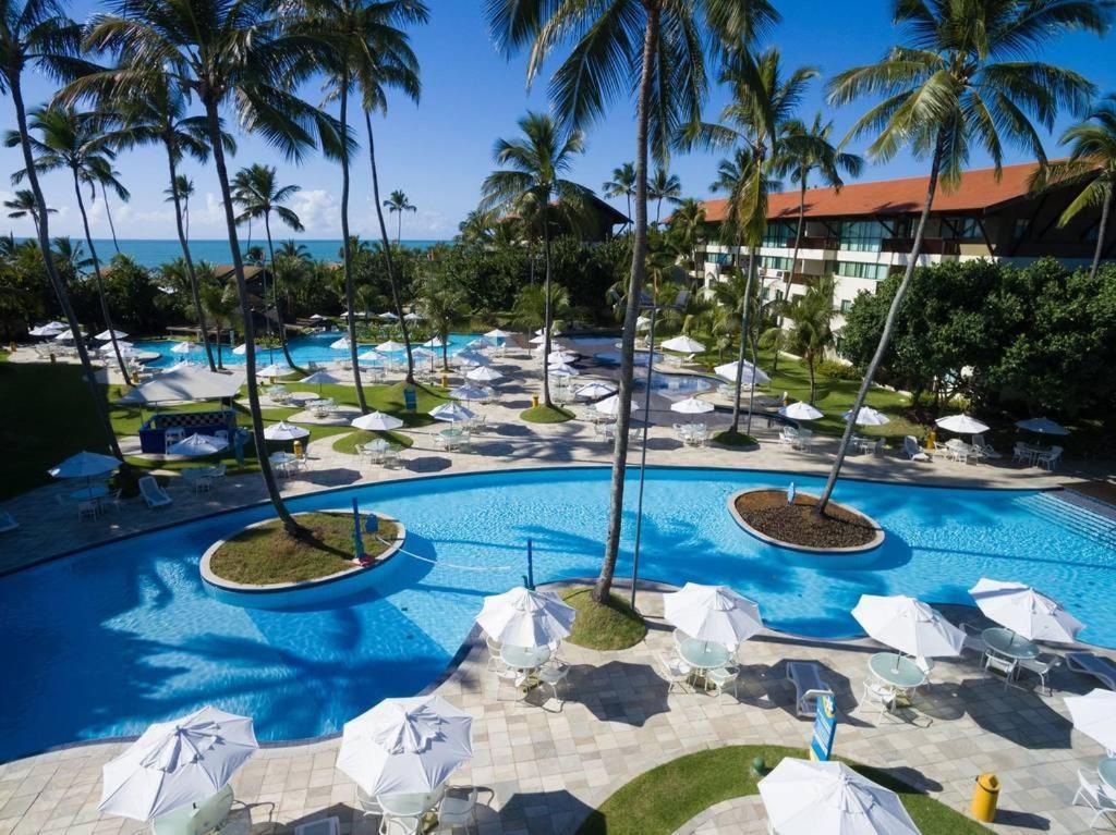 einen Pool im Resort mit Sonnenschirmen und Palmen in der Unterkunft Marulhos Resort Flat E205 in Porto De Galinhas