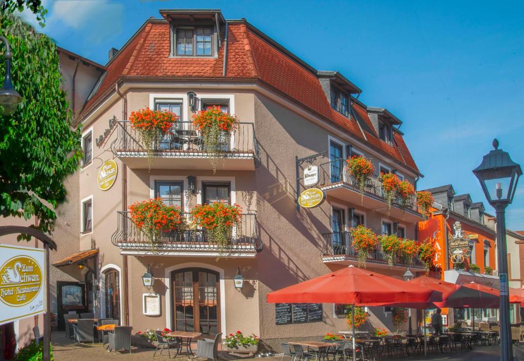 a building with flowers on the balconies and tables and an umbrella at Hotel Restaurant Zum Schwan in Mettlach