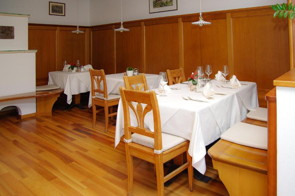 uma sala de jantar com uma mesa com mesas e cadeiras brancas em Berggasthof Locanda Alpina Dorfner em Montagna