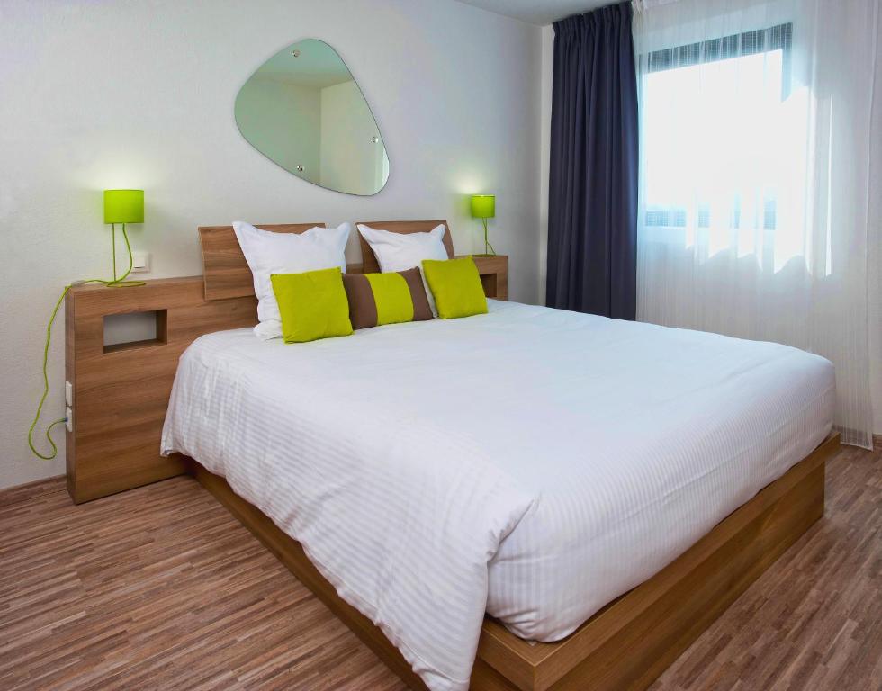 una camera da letto con un grande letto bianco con cuscini gialli di Ténéo Apparthotel Bordeaux Mérignac Aéroport a Mérignac