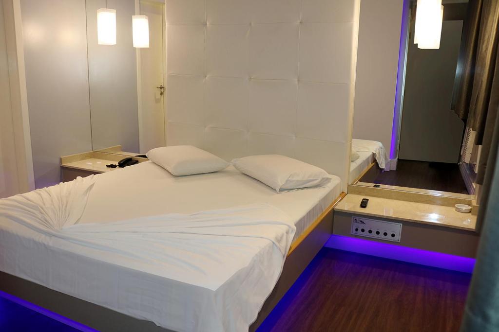 a bedroom with a white bed with purple lights at Hotel Praia Grande Niterói in Niterói
