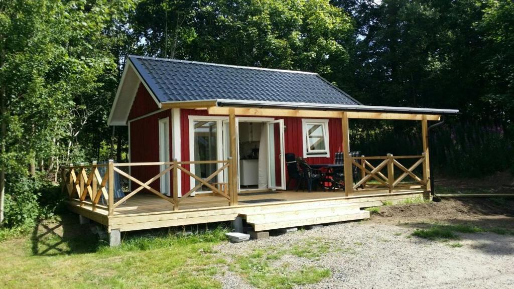 une petite maison rouge avec une terrasse couverte dans un champ dans l'établissement Sjönära Ullared, à Ullared