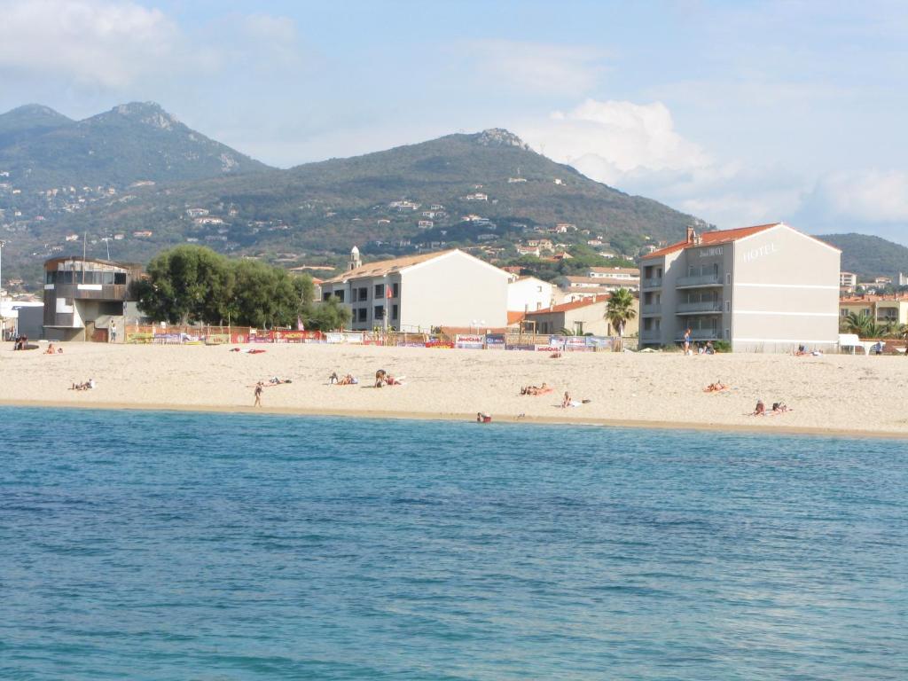 a beach with people on the sand and buildings at Hôtel Beach in Propriano