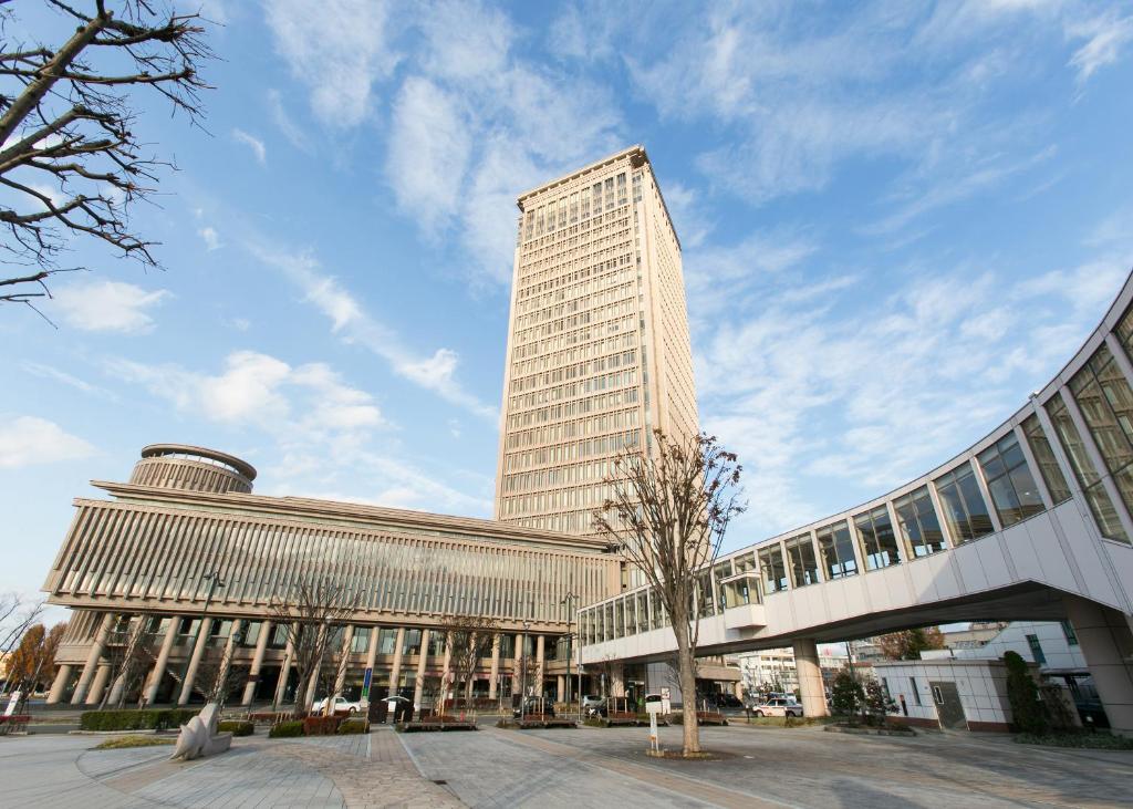 een groot hoog gebouw met een boom ervoor bij Yamagata Eki Nishiguchi Washington Hotel in Yamagata