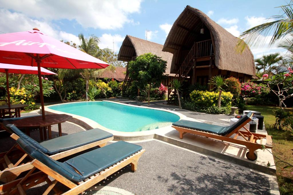 a resort with a swimming pool with chairs and an umbrella at Rambo Homestay in Uluwatu