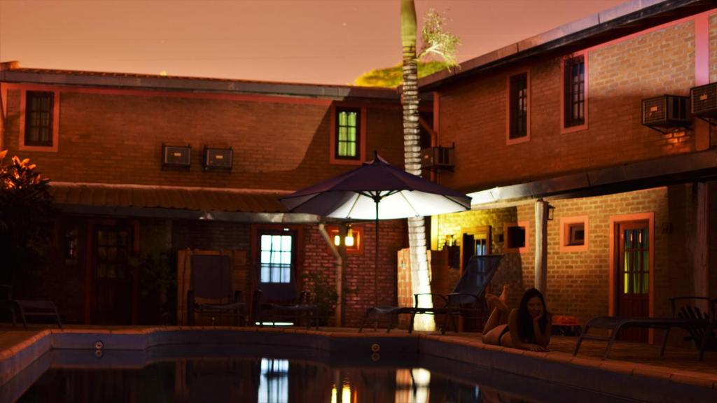 a woman sitting under an umbrella next to a pool at marangatu apart hotel in Puerto Iguazú