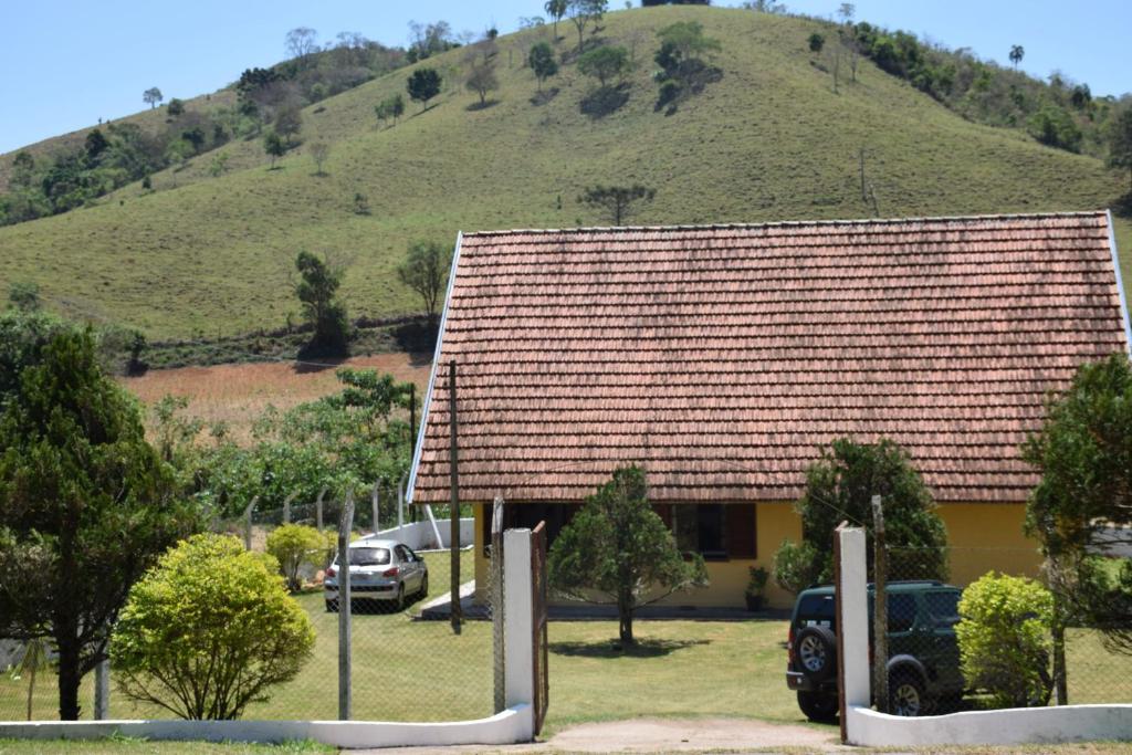 a house with a mountain in the background with cars parked in front at Sitio Sao Francisco de Assis in Santo Antônio do Pinhal