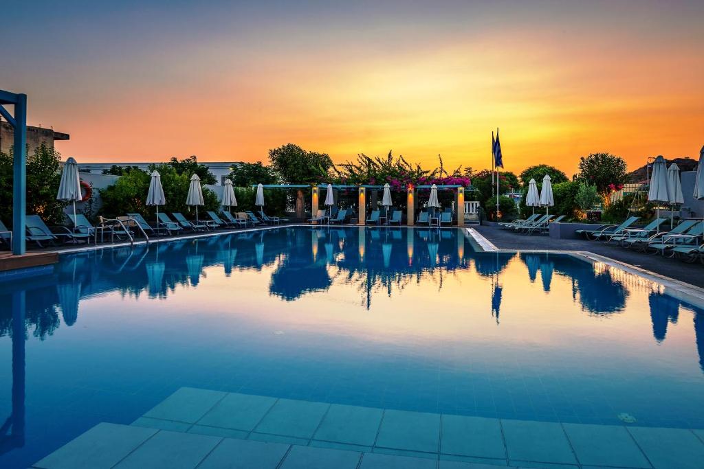 a swimming pool with chairs and umbrellas at sunset at Nissia Kamares in Kardamaina