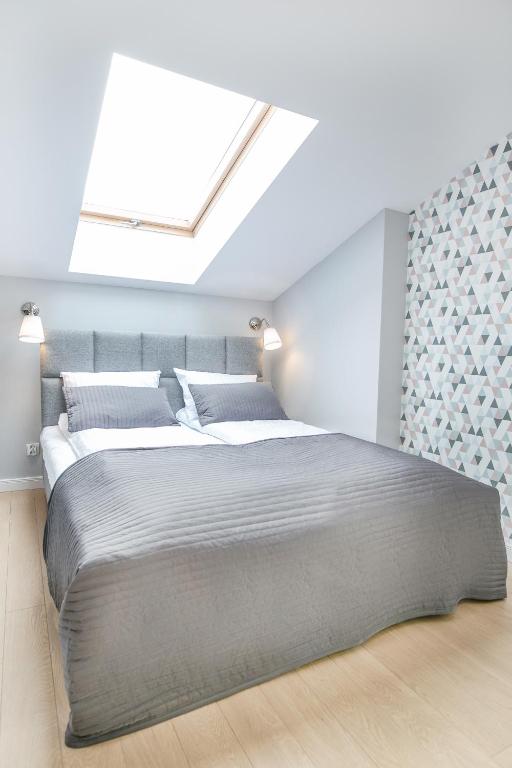 Bright bedroom beneath skylight with grey quilted bedspread and subtle geometric accent wallpaper.