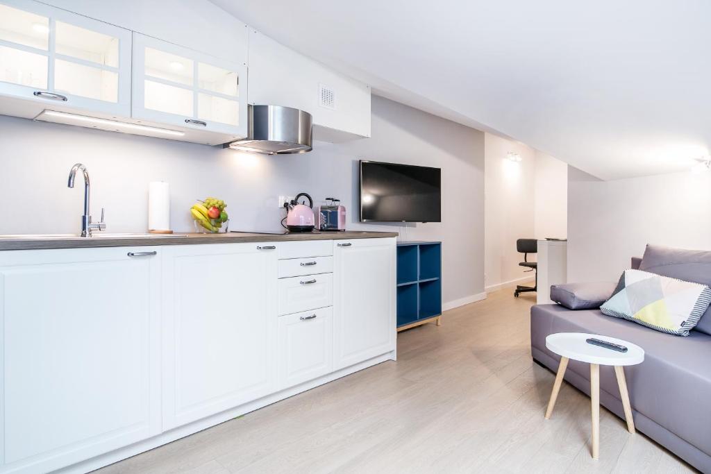 Open-plan living and kitchen with white cabinetry, grey sofa, wall-mounted TV and small round table.