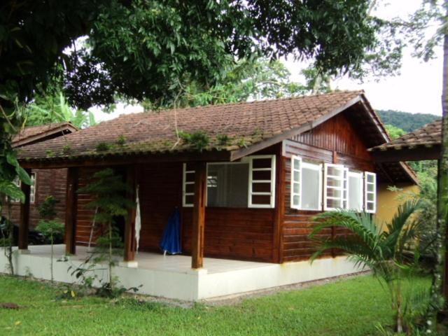 a small wooden house with white windows and a yard at Casa Condomínio Boiçucanga in Boicucanga