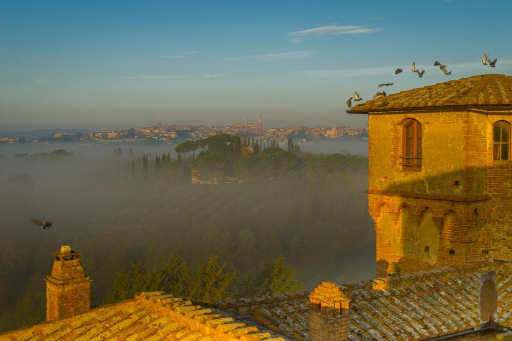 an old building with birds flying over a foggy city at Castello Delle Quattro Torra in Siena