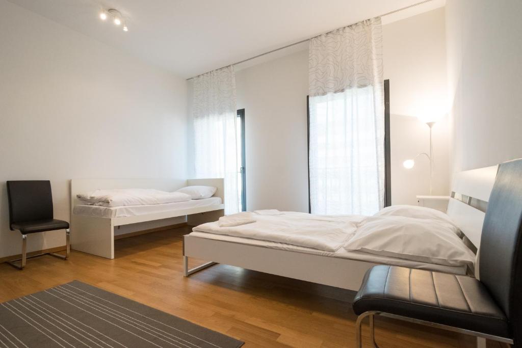 a white bedroom with two beds and a chair at Mainhatten Apartment in Frankfurt/Main