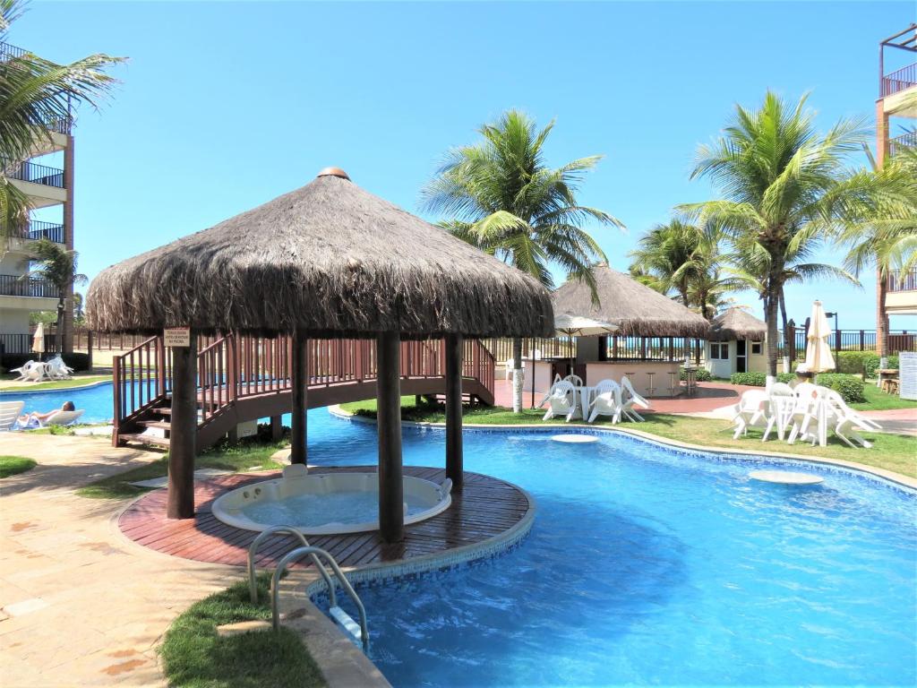 uma piscina com um guarda-sol de palha e um resort em Beach Living em Aquiraz