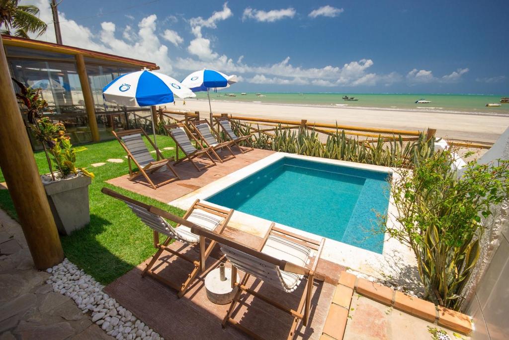 a swimming pool with chairs and umbrellas next to a beach at Ecohar Yoga (Vegetariano & Vegano) in Maragogi