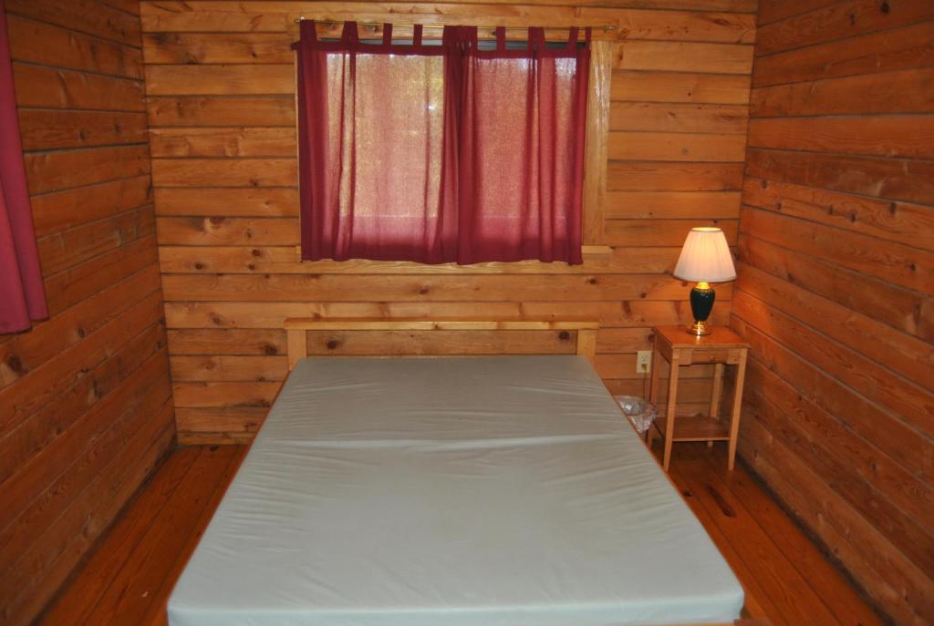 Bett in einem Zimmer mit Fenster und Lampe in der Unterkunft Robin Hill Camping Resort Two-Bedroom Cottage 6 in Lenhartsville