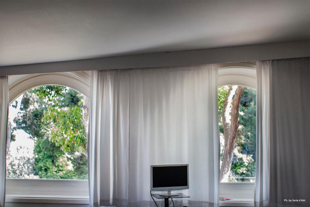 een kamer met 2 ramen met witte gordijnen en een tv bij Residenza Le Rose Villa D'Arte in Napels