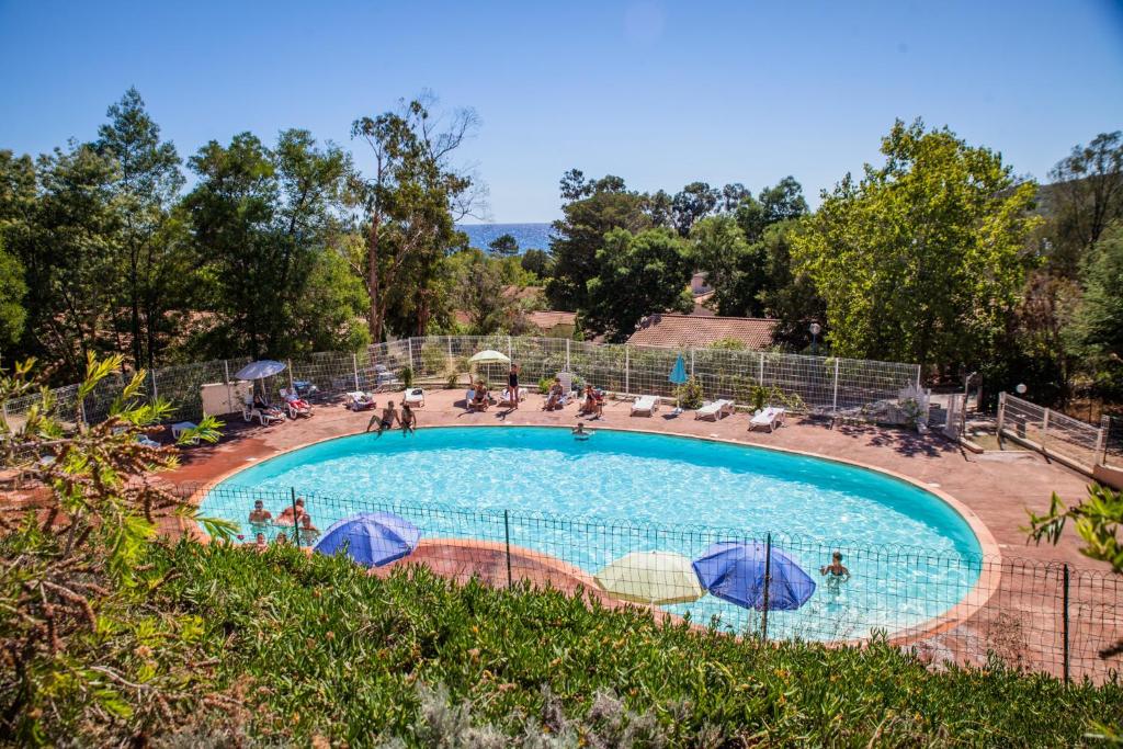 a swimming pool with umbrellas and people sitting around it at Vacancéole - Résidence Lisa Maria in Favone