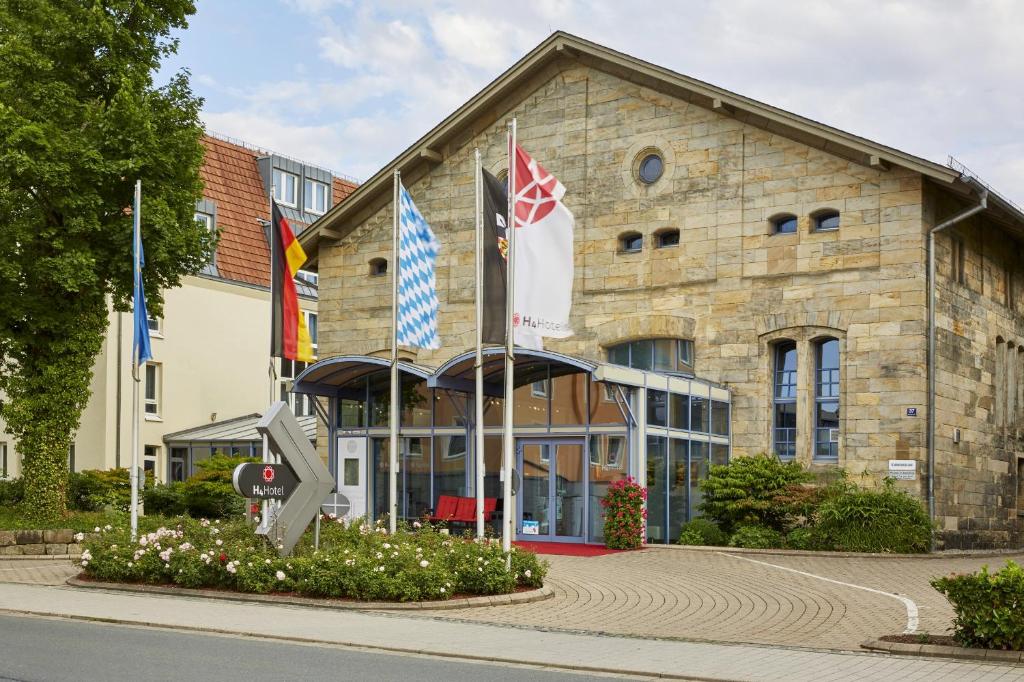 un bâtiment avec drapeaux devant lui dans l'établissement H4 Hotel Residenzschloss Bayreuth, à Bayreuth