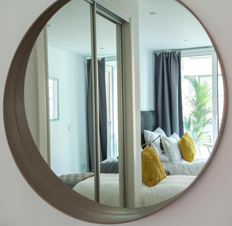 Vetrelax Chelmsford Apartment في تشيلمسفورد: مرآة تعكس غرفة نوم مع سرير مع الوسائد الصفراء