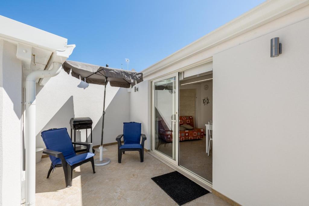 un patio con 2 sillas azules y una sombrilla en Marinella di Montalbano, en Punta Secca