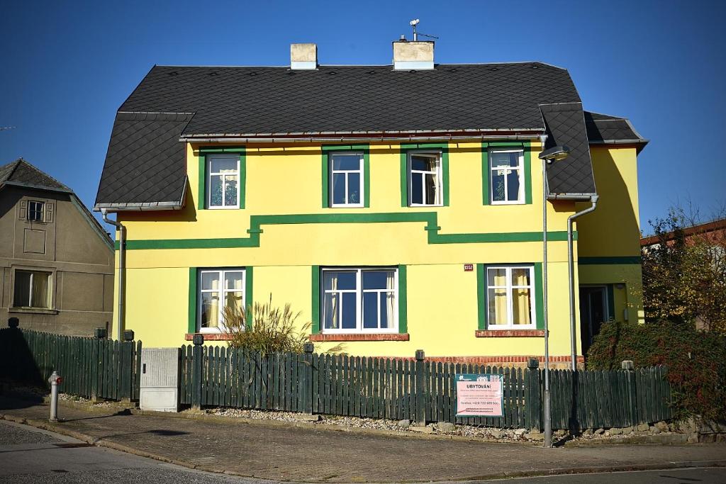 une maison jaune avec un toit noir et une clôture dans l'établissement Penzion Slunečnice, à Dvůr Králové nad Labem