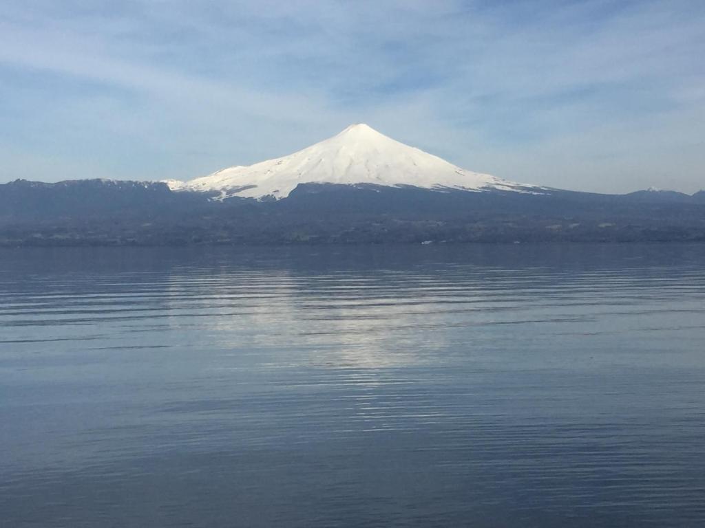 una montaña cubierta de nieve sobre un cuerpo de agua en Cabaña Lago Villarrica ideal 2 familias, en Villarrica